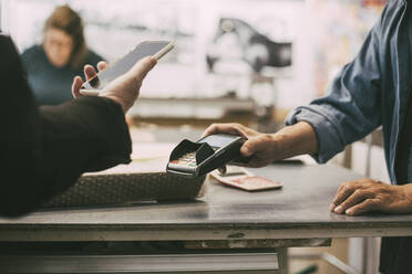 Cropped hand of female customer doing contactless payment at retail shop - MASF26479