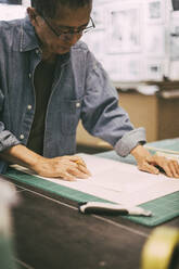 Senior craftsman examining paper while working in shop - MASF26509