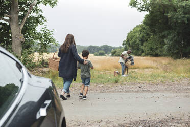 Rückansicht einer Frau, die mit ihrem Sohn beim Picknick auf die Familie zugeht - MASF26522