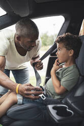 Father talking with son while fastening seat belt in car - MASF26533