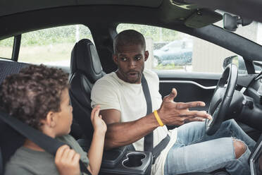 Boy talking with father while sitting in electric car - MASF26536