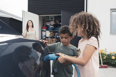 Sister and brother charging electric car at front yard - MASF26570