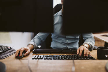 Geschäftsmann, der einen Computer benutzt, während er am Schreibtisch im Büro sitzt - MASF26575