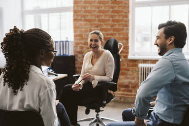 Female and male professionals laughing while discussing in office - MASF26590