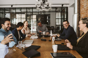 Fröhliche Geschäftsleute, die lachend am Konferenztisch im Sitzungssaal sitzen - MASF26607
