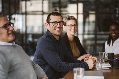 Portrait of mid adult businessman sitting amidst colleagues at conference table - MASF26609