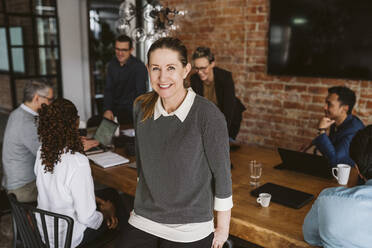 Portrait of smiling business professional standing while colleagues discussing in background - MASF26616