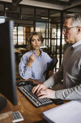 Female professional discussing with businessman using computer at desk - MASF26663