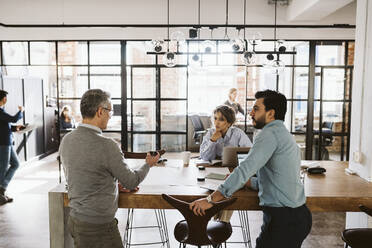 Male and female colleagues looking at mature businessman explaining in creative office - MASF26678