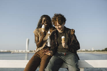 Jugendlicher und junge Frau halten Eis, während sie auf einem Geländer sitzen - MASF26696