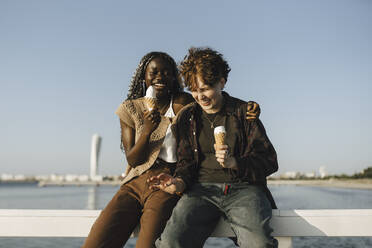 Teenage boy and young woman holding ice cream while sitting on railing - MASF26696