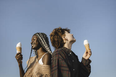 Smiling teenage boy and young woman holding ice cream cones against clear sky - MASF26699