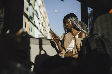 Junge Frau benutzt Smartphone im Bus an einem sonnigen Tag - MASF26705