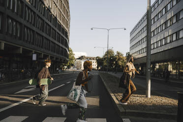 Glückliche multirassische Freunde laufen beim Überqueren der Straße in der Stadt - MASF26708