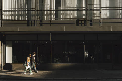 Teenage boy and non-binary woman walking on footpath in city - MASF26716