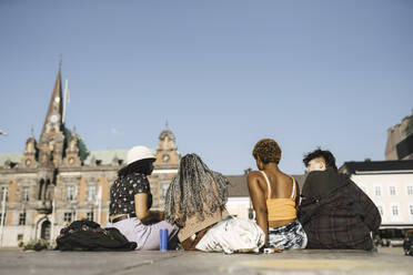 Oberflächenniveau Ansicht von multirassischen Freunden sitzen in der Stadt an einem sonnigen Tag - MASF26720