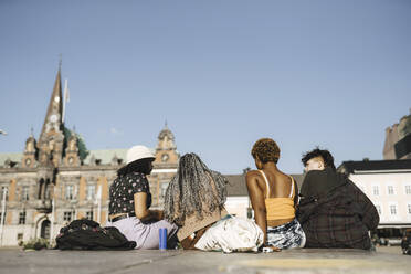 Surface level view of multiracial friends sitting in city on sunny day - MASF26720