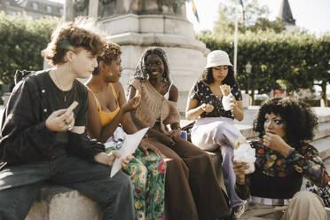 Smiling friends eating food on retaining wall - MASF26724