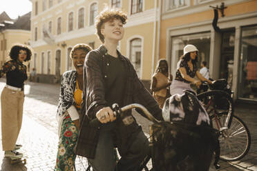 Cheerful friends cycling and skateboarding on street in city - MASF26731