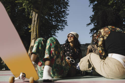 Young transgender with skateboard lying by female friends in park on sunny day - MASF26739