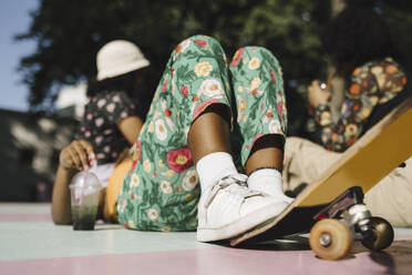 Junge nicht-binäre Person liegt mit Skateboard und Freunden in einem Park an einem sonnigen Tag - MASF26740