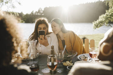 Junge Frau benutzt ihr Smartphone, während sie mit Freundinnen auf einer Party sitzt - MASF26790