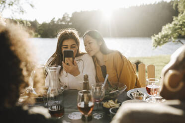 Young woman using smart phone while sitting with female friends at party - MASF26790