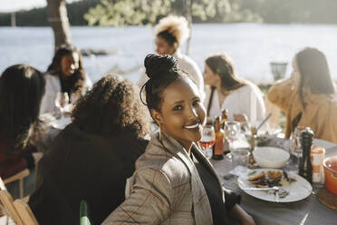 Porträt einer lächelnden Frau, die mit Freundinnen auf einer Dinnerparty an einem sonnigen Tag sitzt - MASF26803