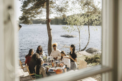 Fröhliche Freundinnen genießen eine Dinnerparty durch ein Fenster gesehen - MASF26806