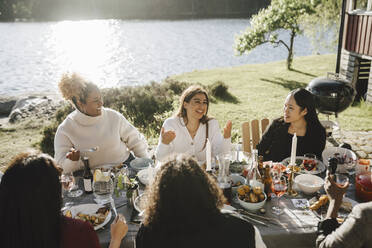Glückliche Frau im Gespräch mit weiblichen Freunden, während sie eine Dinnerparty im Hinterhof an einem sonnigen Tag genießt - MASF26807