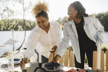 Smiling female friends arranging table on sunny day - MASF26827