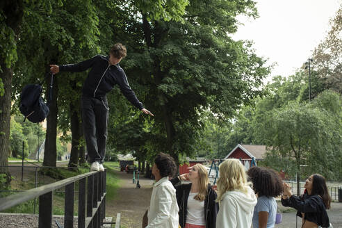 Teenager, der auf einem Geländer läuft, während seine Freunde und Freundinnen ihn im Park beobachten - MASF26860