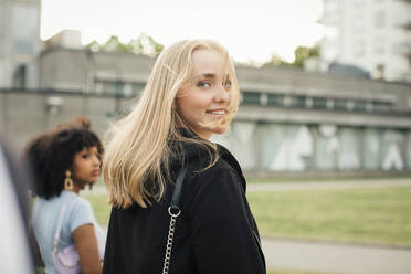 Lächelndes Teenager-Mädchen, das mit einer Freundin im Park spazieren geht - MASF26871