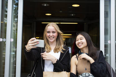 Lächelnde Freundinnen machen ein Selfie mit ihrem Smartphone im Einkaufszentrum - MASF26912