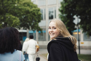 Smiling teenage girl looking over shoulder while walking with friends - MASF26917