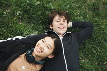 Lächelnde männliche und weibliche Freunde liegen im Gras - MASF26963
