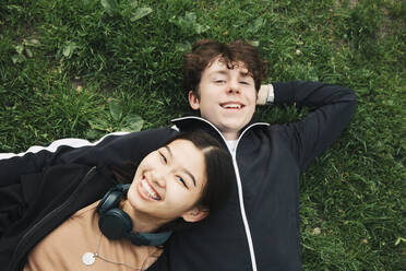 Smiling male and female friends lying on grass - MASF26963