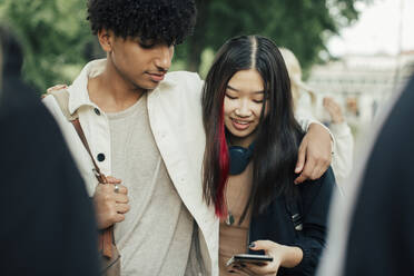 Teenager-Mädchen benutzt Smartphone beim Spaziergang mit einem männlichen Freund im Park - MASF26966