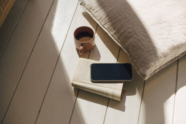 Sunlight on book, smart phone, coffee cup and cushion on floor at home - MASF26972