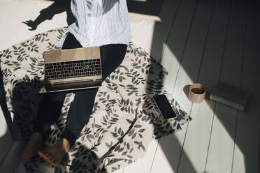 Ausgeschnittenes Bild einer Frau, die mit einem Laptop auf dem Boden im Sonnenlicht zu Hause sitzt - MASF26976