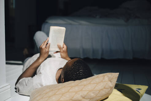 Ein Mann liest ein Buch, während er zu Hause im Sonnenlicht auf dem Boden liegt - MASF26981