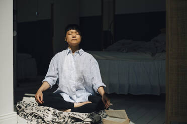 Young woman meditating in sunlight at home - MASF26982