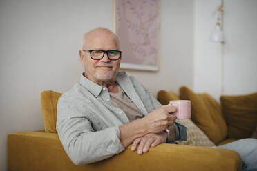 Porträt eines älteren Mannes mit Kaffeetasse, der zu Hause auf dem Sofa sitzt - MASF26993