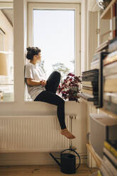Junge Frau sitzt zu Hause am Fenster - MASF27004