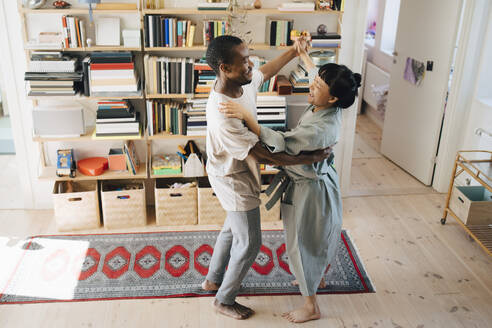 Lächelnde multirassische Paar tanzen zusammen im Wohnzimmer zu Hause - MASF27036