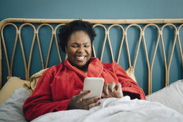 Happy mid adult woman using smart phone on bed at home - MASF27055