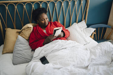 Lächelnde Frau liest ein Buch auf dem Bett zu Hause - MASF27058