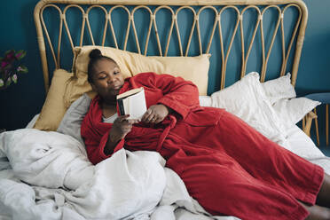 Mid adult woman reading book while relaxing on bed - MASF27060