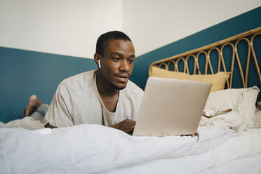 Mid adult man using laptop over bed in bedroom - MASF27066