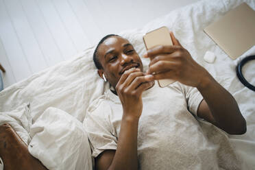 Smiling mid adult man using mobile phone while lying on bed - MASF27068